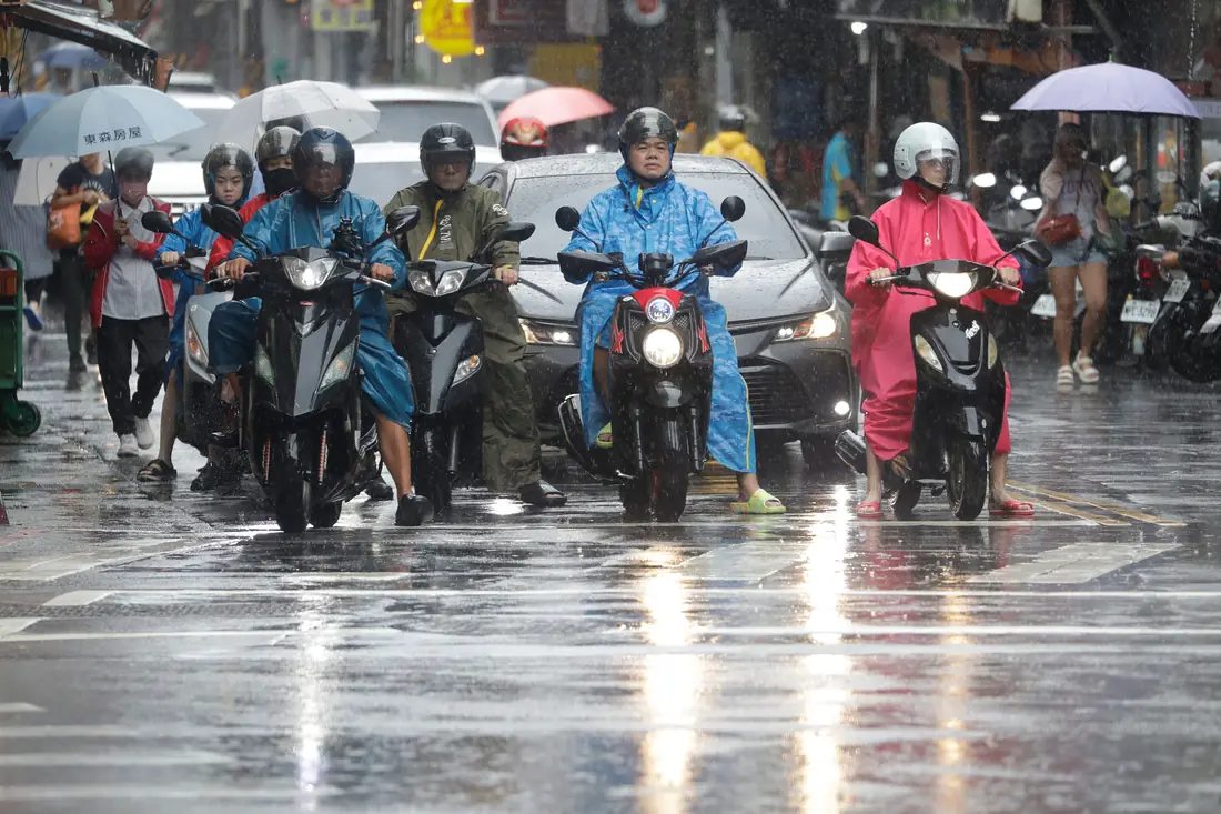 People ride scooters in rain as Typhoon Champi approaches Taipei, October 23, 2026. Not a photograph of an airport closure.